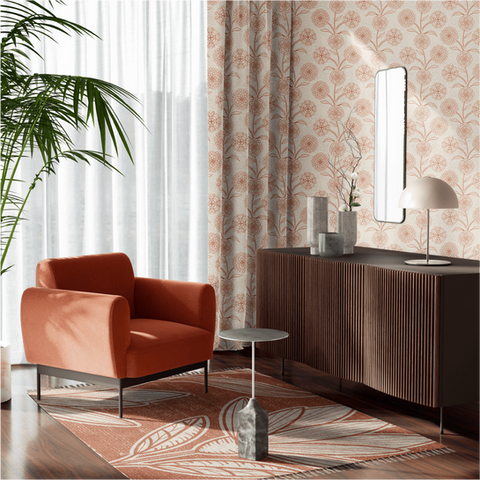 A stylish living room corner featuring terracotta armchair, dark wooden sideboard with decor items, oval mirror above it, geometric-patterned area rug on floor, floral wallpapered walls, sheer curtains over window allowing natural light inside next to an indoor plant.