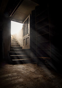 Dark and creepy wooden cellar door open at bottom of old stone stairs bright sun light ray