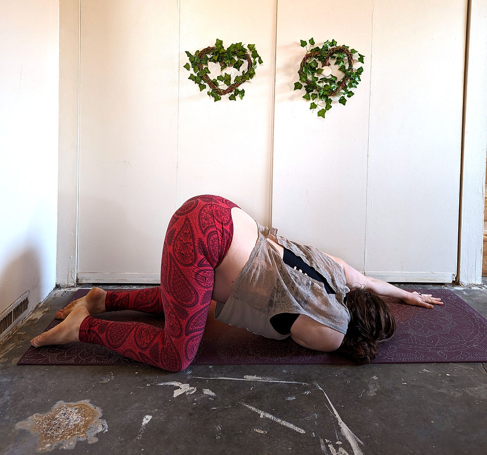 Person on a yoga mat in a thread the needle stretch before a white wall with two green heart wreaths.
