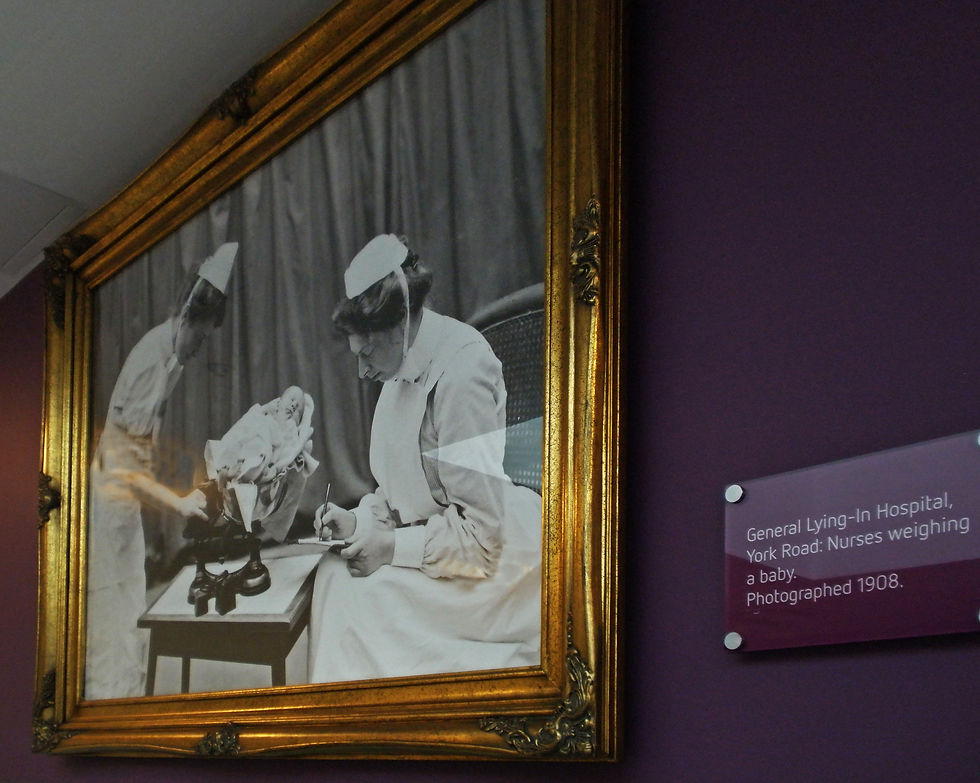 Framed black-and-white photo of nurses weighing a baby, beside a plaque reading General Lying-In Hospital, York Road, photographed 1908.