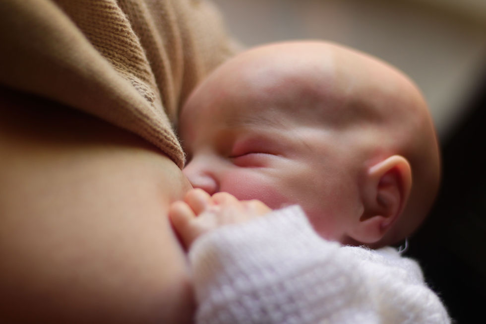 Sleeping newborn nursing at a mother’s breast, close-up with soft warm tones and a calm, tender mood