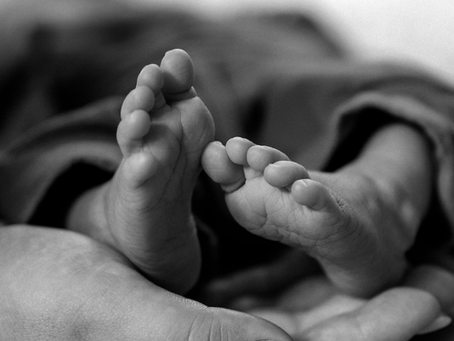 Black-and-white close-up of a baby's feet resting in an adult's hands, soft and tender.