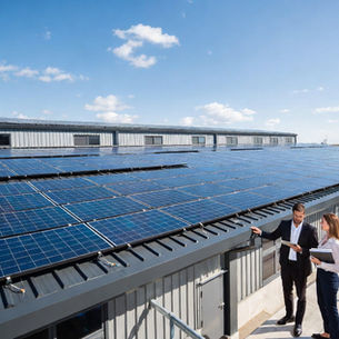 Chef d’entreprise et ingénieur énergie discutant devant une grande installation de panneaux solaires photovoltaïques sur la toiture d’un bâtiment industriel moderne, documents et tablette affichant projet solaire, environnement industriel propre et moderne, panneaux solaires brillants au soleil, photographie professionnelle ultra réaliste d’infrastructure énergétique durable et énergie renouvelable pour entreprises B2B
