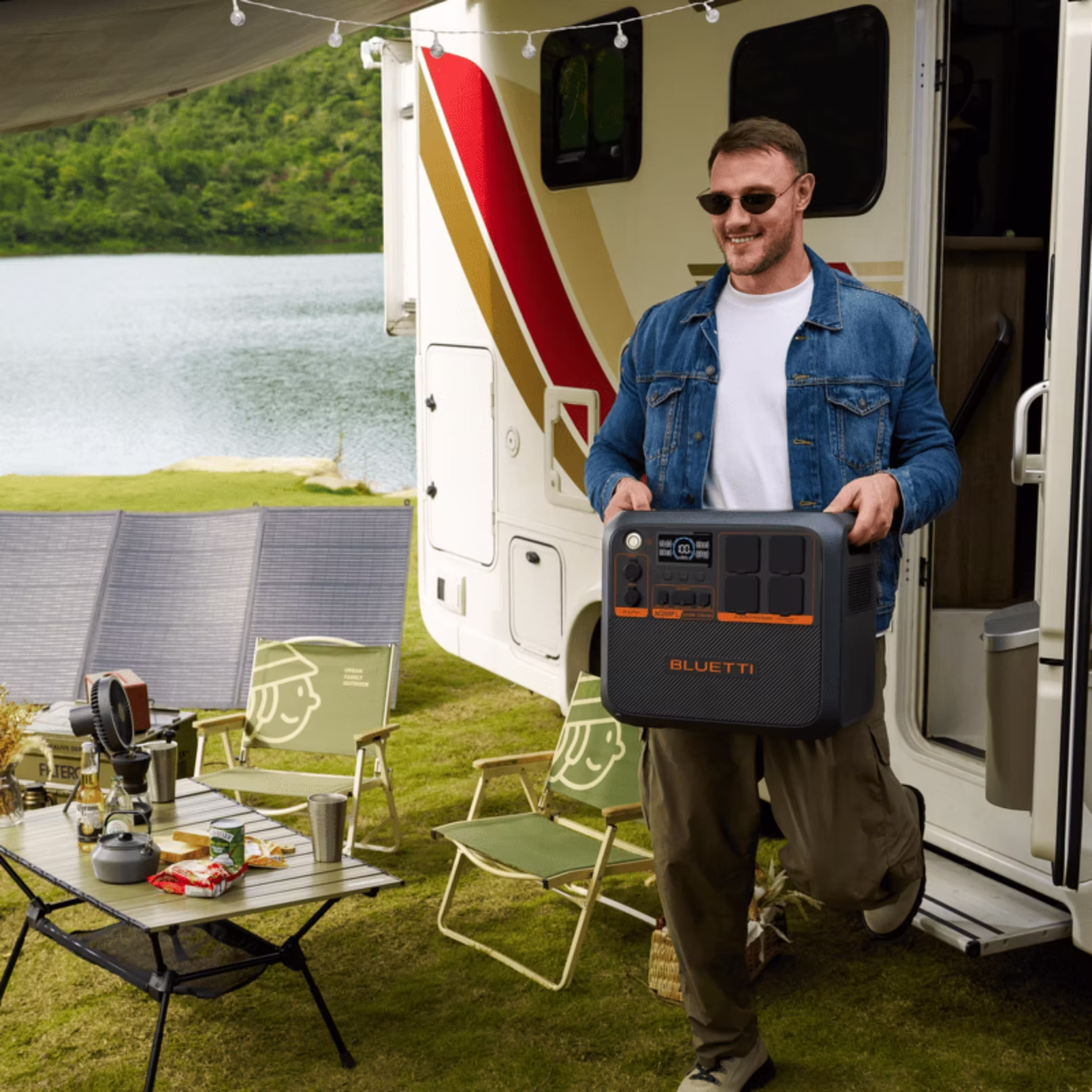 Station électrique BLUETTI Premium 200 tenue par un utilisateur devant un camping-car, avec un espace extérieur aménagé près d’un lac.