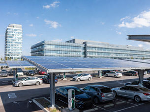 Grand parking d’entreprise équipé d’ombrières photovoltaïques modernes avec panneaux solaires sur structures métalliques, voitures stationnées sous les ombrières, bornes de recharge pour véhicules électriques, bâtiment tertiaire en arrière-plan, ciel bleu lumineux, photographie ultra réaliste d’infrastructure énergétique durable et énergie renouvelable pour entreprises B2B