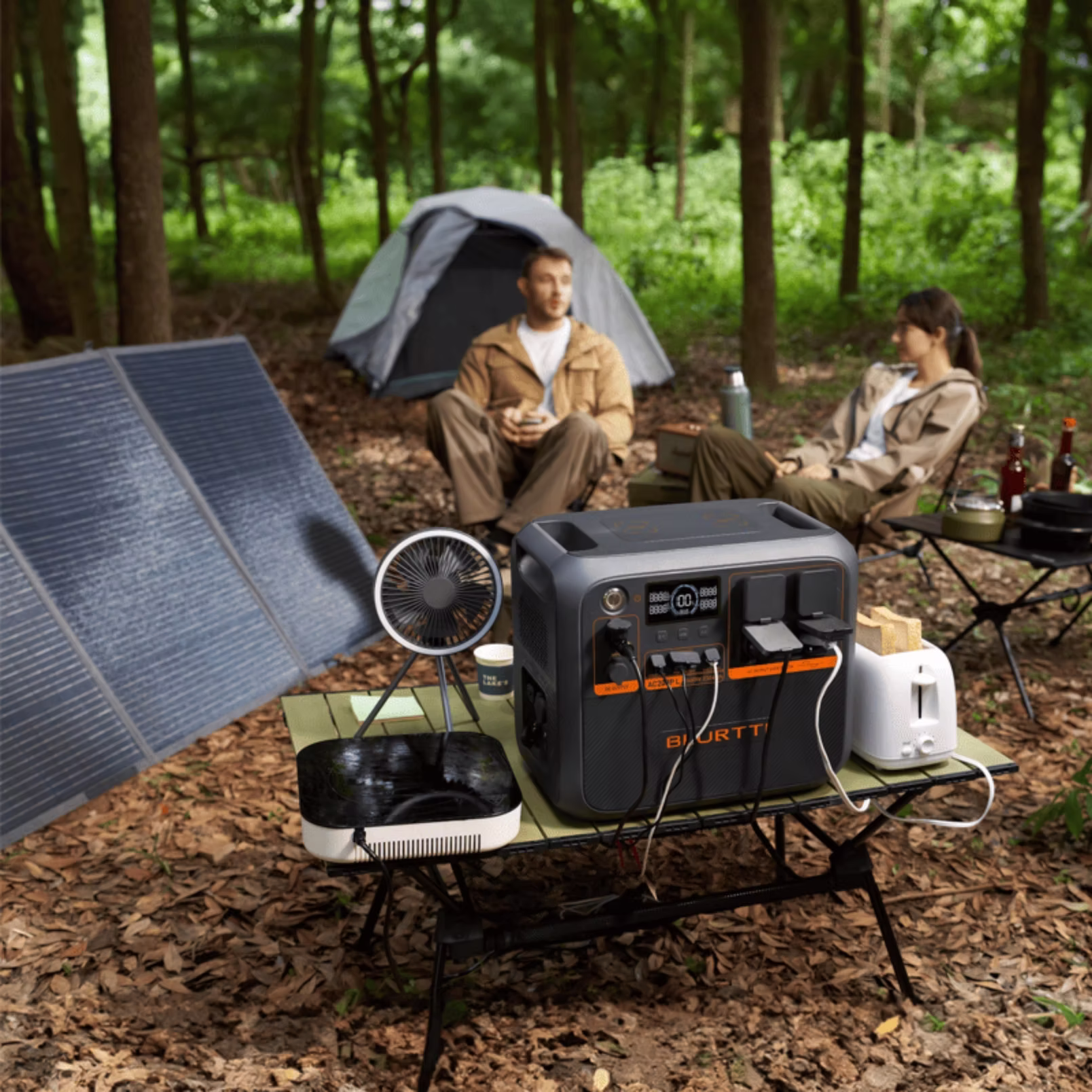 « Station électrique BLUETTI Premium 200 utilisée en camping en forêt, posée sur une table avec panneaux solaires déployés et deux campeurs assis près d’une tente.
