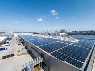 Grande usine moderne en zone industrielle française avec immense toiture entièrement recouverte de panneaux solaires photovoltaïques, camions et bâtiments logistiques, panneaux solaires brillants au soleil, architecture industrielle contemporaine, photographie ultra réaliste d’infrastructure énergétique durable et énergie renouvelable pour entreprises B2B