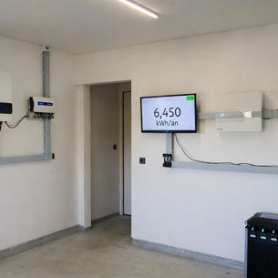 Garage technique d’une maison en Pays de la Loire avec onduleur Huawei SUN2000 et onduleur hybride Sungrow fixés au mur, batterie domestique raccordée au tableau électrique, câblage soigné et écran de monitoring indiquant une production solaire annuelle de 6 450 kWh, installation photovoltaïque résidentielle haute performance.