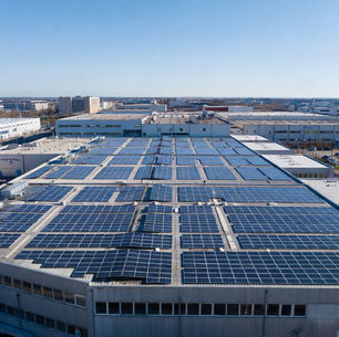 Usine industrielle moderne en France équipée de panneaux solaires photovoltaïques sur toute la toiture, zone industrielle avec bâtiments d’entreprise et parkings, énergie solaire durable sous ciel bleu, photographie réaliste d’architecture technologique et photovoltaïque