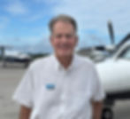 Paul is wearing a casual white button up with Viral Flight logo and standing in front of a small plane.