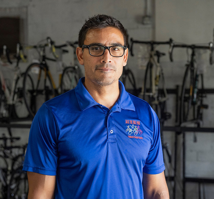 Alex is wearing black square eyeglasses and a blue Jack the Bike Man dri fit polo.