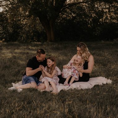 Photo of a family of four looking happy and having a picnic in a meadow. Natural, storytelling photography by Suffolk photographer Mikaela Jade.