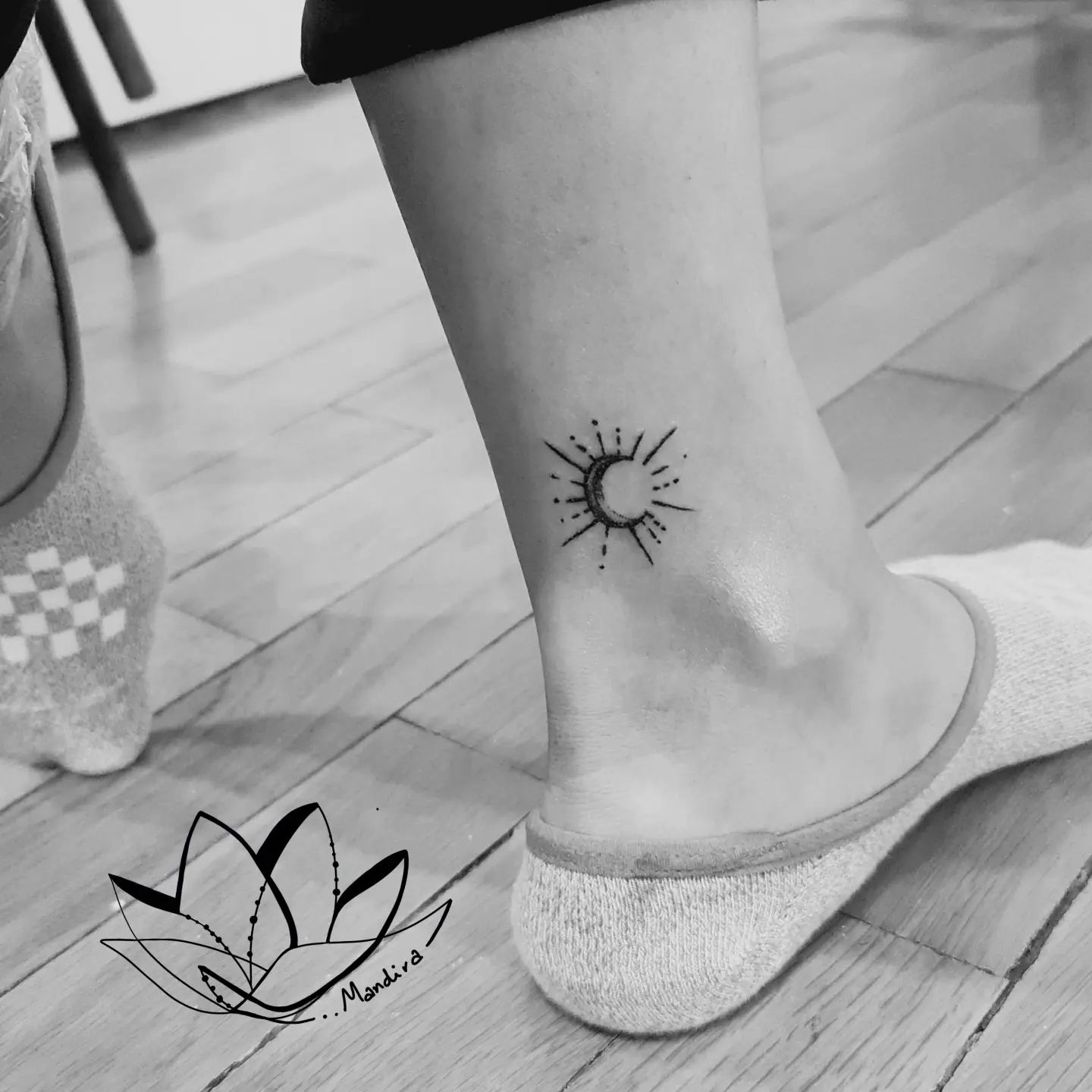 A small crescent moon, shaded with dotting, with rays around it . A cute tattoo, placed in the upper ankle, black ink