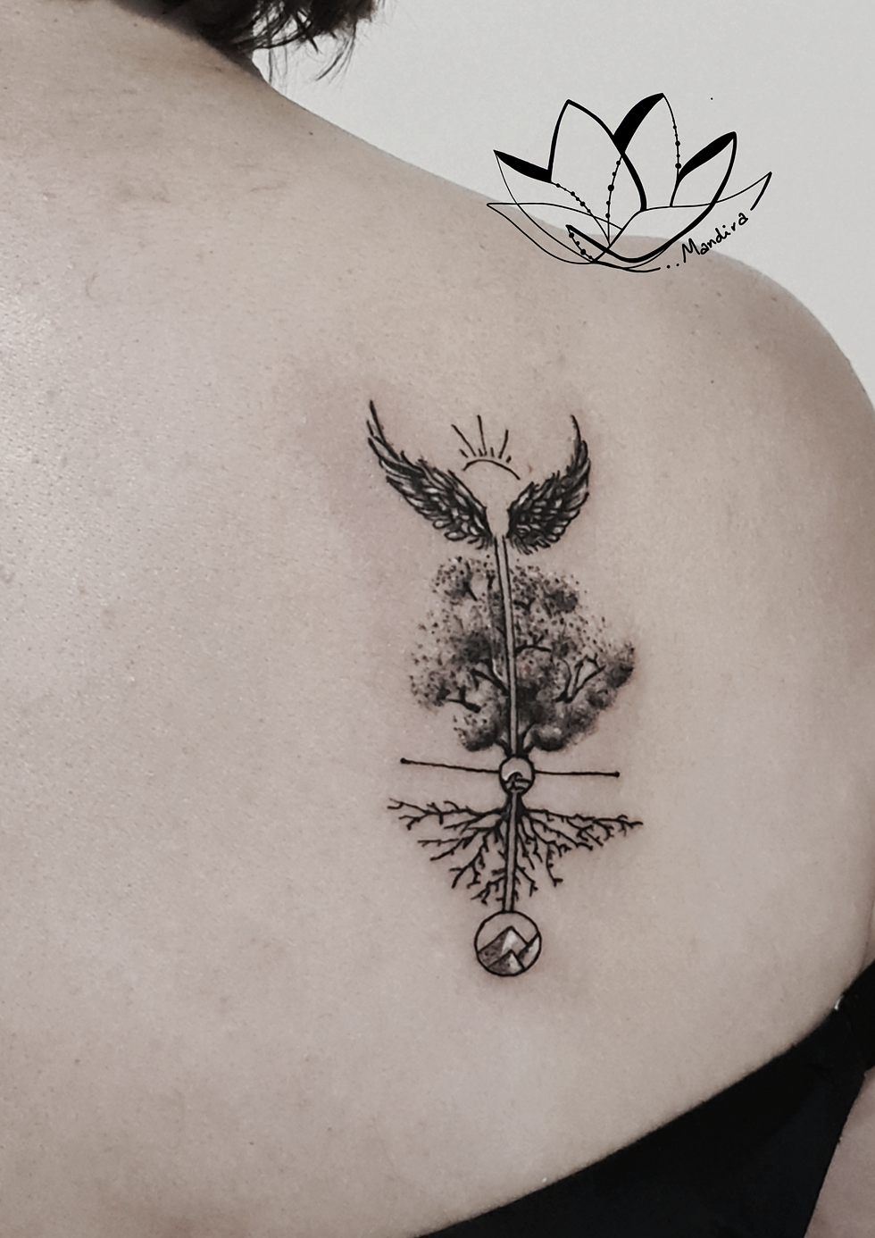 A tree of life design with angel wings and sun rays on the top tattooed on the upper right back of a woman. In the middle of the design a wave in a circle and under the roots mountains in a circle.