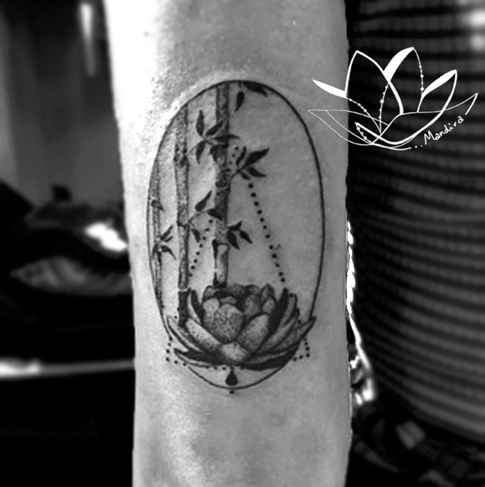 Arm tattoo with a lotus and bamboo tree leaves in simple and dotting style, placed in an oval shape symbolizing rebirth and regeneration