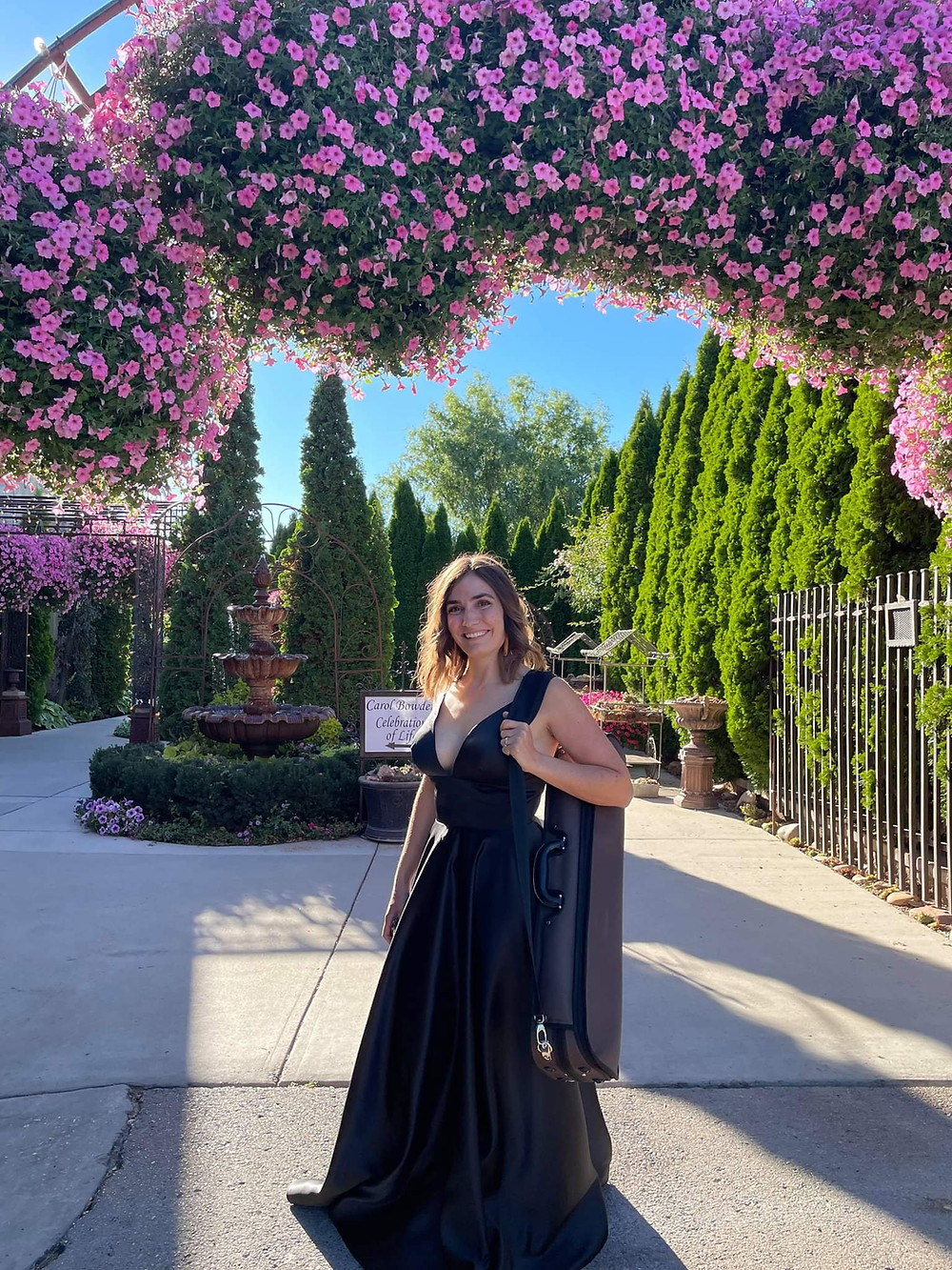 Jessica McAllister, violinist, poses in front of beautiful garden hedge