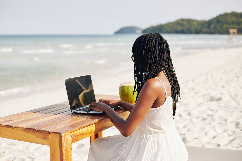 Frau sitzt an einem Schreibtisch am Strand und arbeitet an einem Laptop, umgeben von Sonnenschein, Sand und Meer – Symbol für Workation und flexibles Arbeiten in inspirierender Umgebung