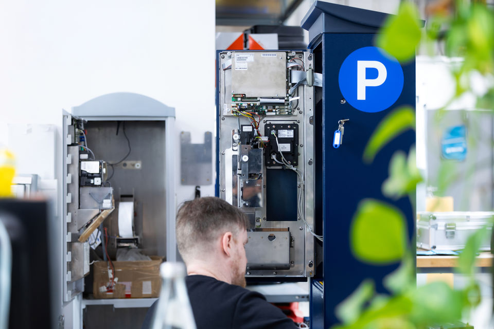 Mann repariert Parkautomat mit "P"-Symbol, interne Komponenten sichtbar.