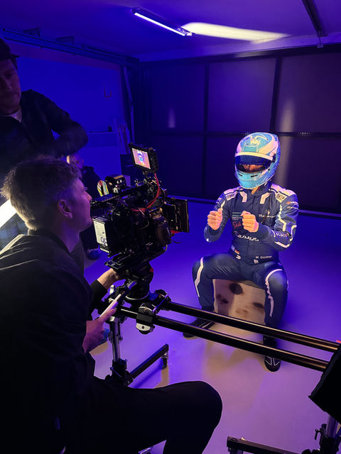 Rennfahrer in blauem Anzug und Helm zeigt Daumen hoch beim Filmdreh.