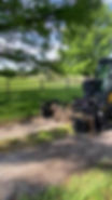 Regrading gravel driveway with heavy equipment near a fence.