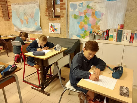 Élèves concentrés sur leur travail d'écriture dans une salle de classe ornée de cartes géographiques.