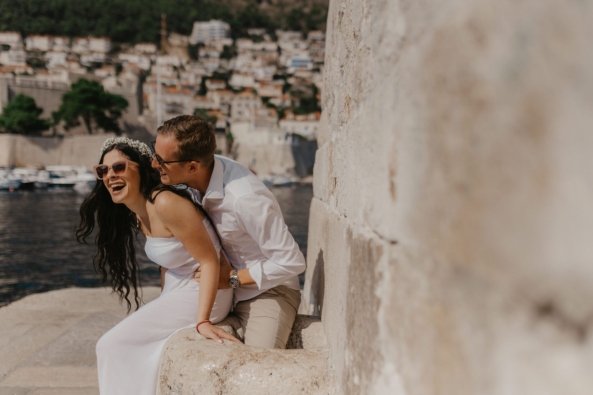the bride and groom are laughing in each other's arms by the water in the harbor of the old town of Dubrovnik