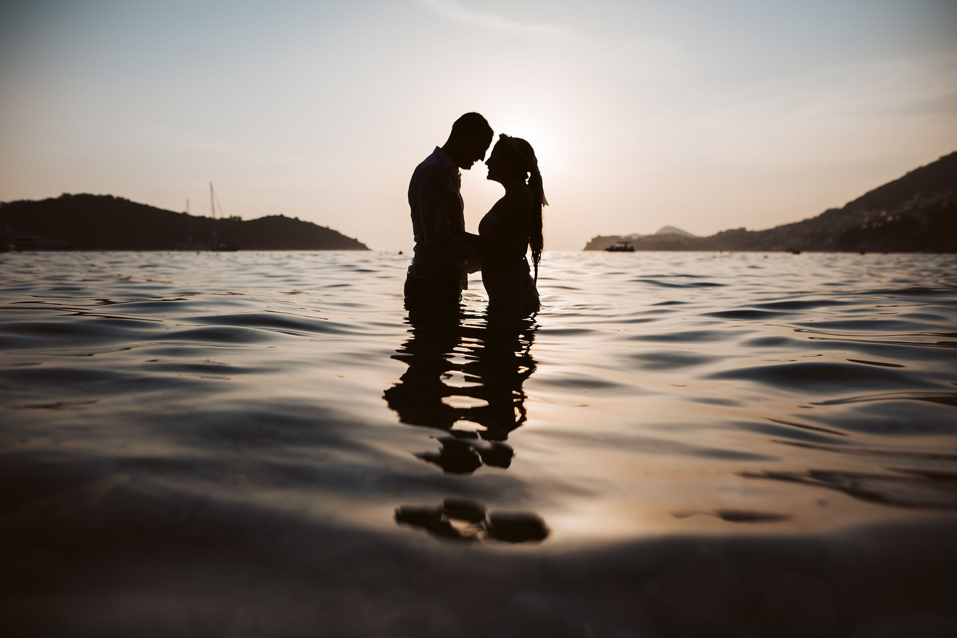 the bride and groom pose halfway in the water in front of St. Jacov's Beach