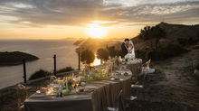 wide-angle documentary photograph of a bride and groom sitting at a luxury decorated wedding table on the cliffside of Park Orsula during a vibrant sunset over Dubrovnik. Photography by Bojan Petričević
