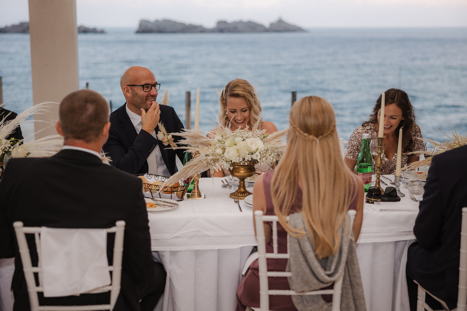 the bride and groom sit with guests at a table on the terrace of a hotel by the sea in Dubrovnik