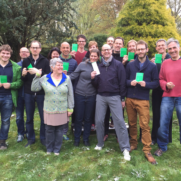 A group of people are standing together in the garden, holding small green certificates in their hands.