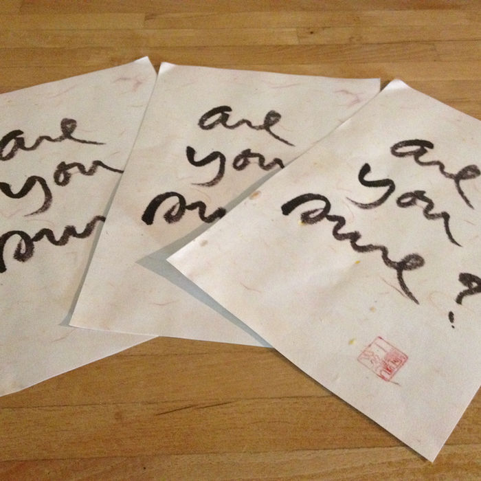 Drei Kalligraphie-Blätter mit dem Schriftzug ‚Are you sure?‘ liegen auf einem Holztisch.
