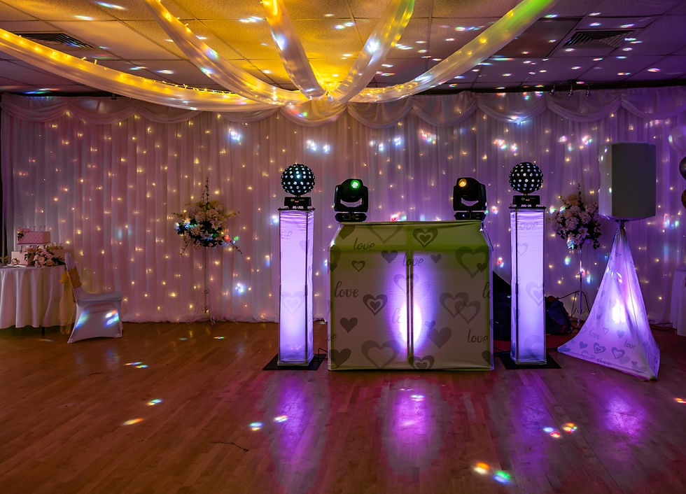 Decorated wedding reception hall with glowing purple DJ booth, heart patterns, draped lights, and disco light reflections