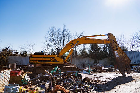Orange excavator with grapple claw is parked next to scrap metal material in active demolition site clean up.