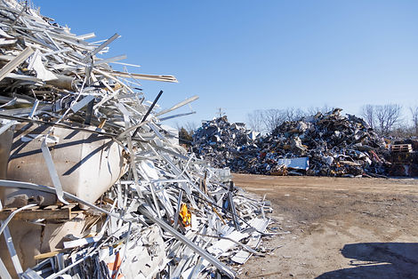 Image shows large scrap piles at their location in Hopkinsville, KY on various types of metal neatly piled 12' and higher. The ground which the piles lay on are clear dirt, and the sky above the piles is bright blue.