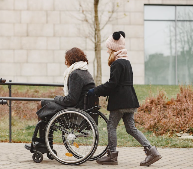 A girl helps push the wheelchair for a wheelchair user