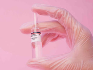 A hand wearing gloves holding a small Covid 19 vaccine bottle