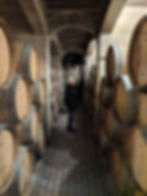 woman poses between rows of wine barrels