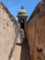 girl holds her hat in a narrow alley of a fort turret