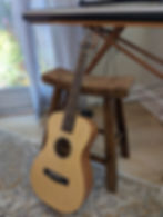 blond guitar leans against a wooden piano stool