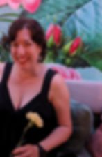 woman in black dress with a carnation and floral wall behind her