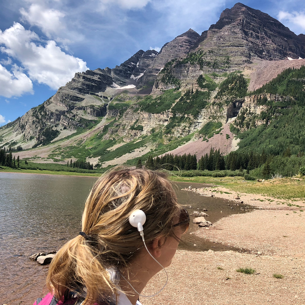 Shannon is at the Maroon Bells Wilderness in colorado. She faces a mountain and her white cochlear implant is prominently displayed on her head.