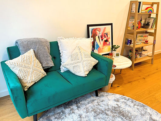 A picture of a green two seater couch with cushions next to a bookshelf