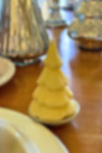 Butter shaped like a Christmas tree on a plate, set on a wooden table with metallic tree decorations in the background. Warm lighting.
