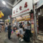 People ordering at a street food stall in an urban area at night. Menu images are displayed overhead. The atmosphere is bustling. Fish balls and Tokyo street food for autheticfood.com