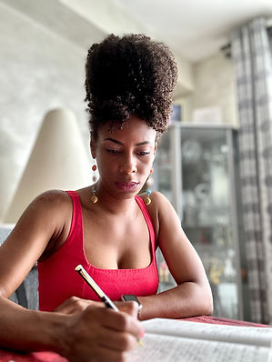Black woman sits at a desk with a pen in hand wears red dress with curly hair in high updo