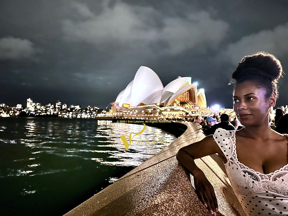Woman in white dress sits with Sydney Opera House in the background at night time after New Year’s Eve celebrations overlooking the Sydney Harbor