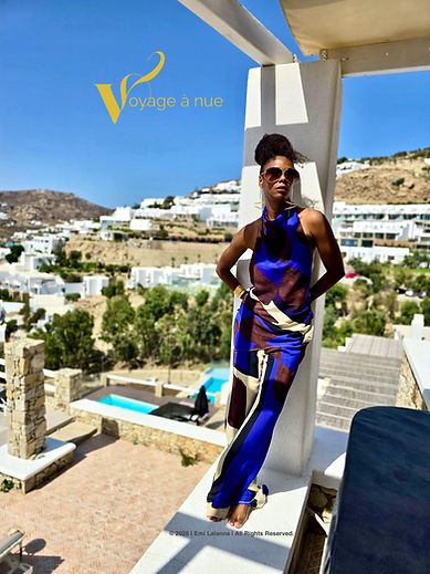 black woman wears gold jewelry stands on balcony in mykonos looks pensively into the sky