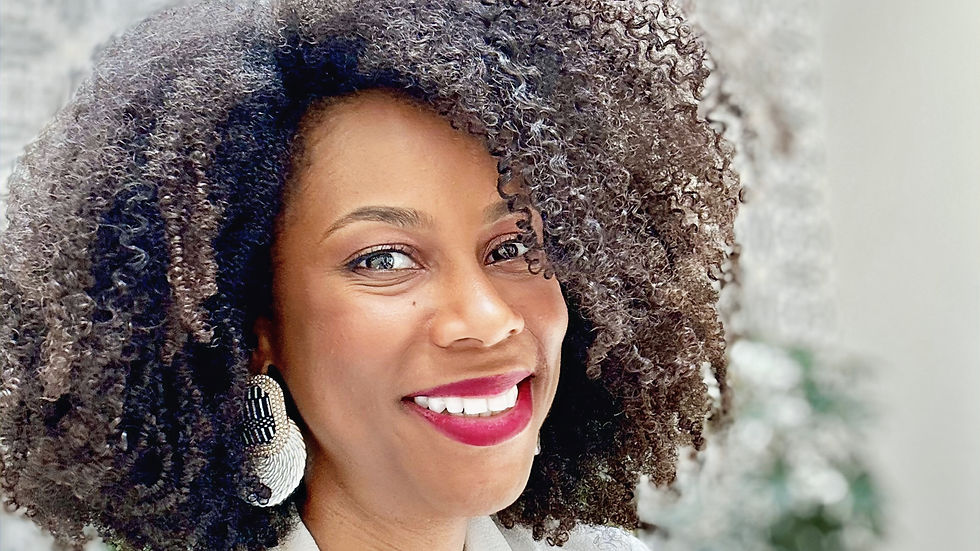 Smiling woman with curly afro hair and vibrant earrings in a white outfit using travel as therapy. Background features black and white Spanish-style patterned wall and hanging plants.