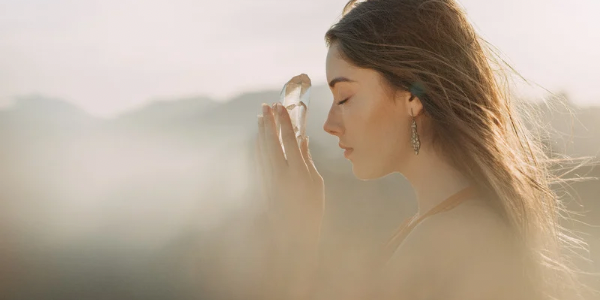 Woman holding a crystal to her forehead in meditation, surrounded by soft golden light and mist, symbolizing clarity, release, and spiritual renewal.