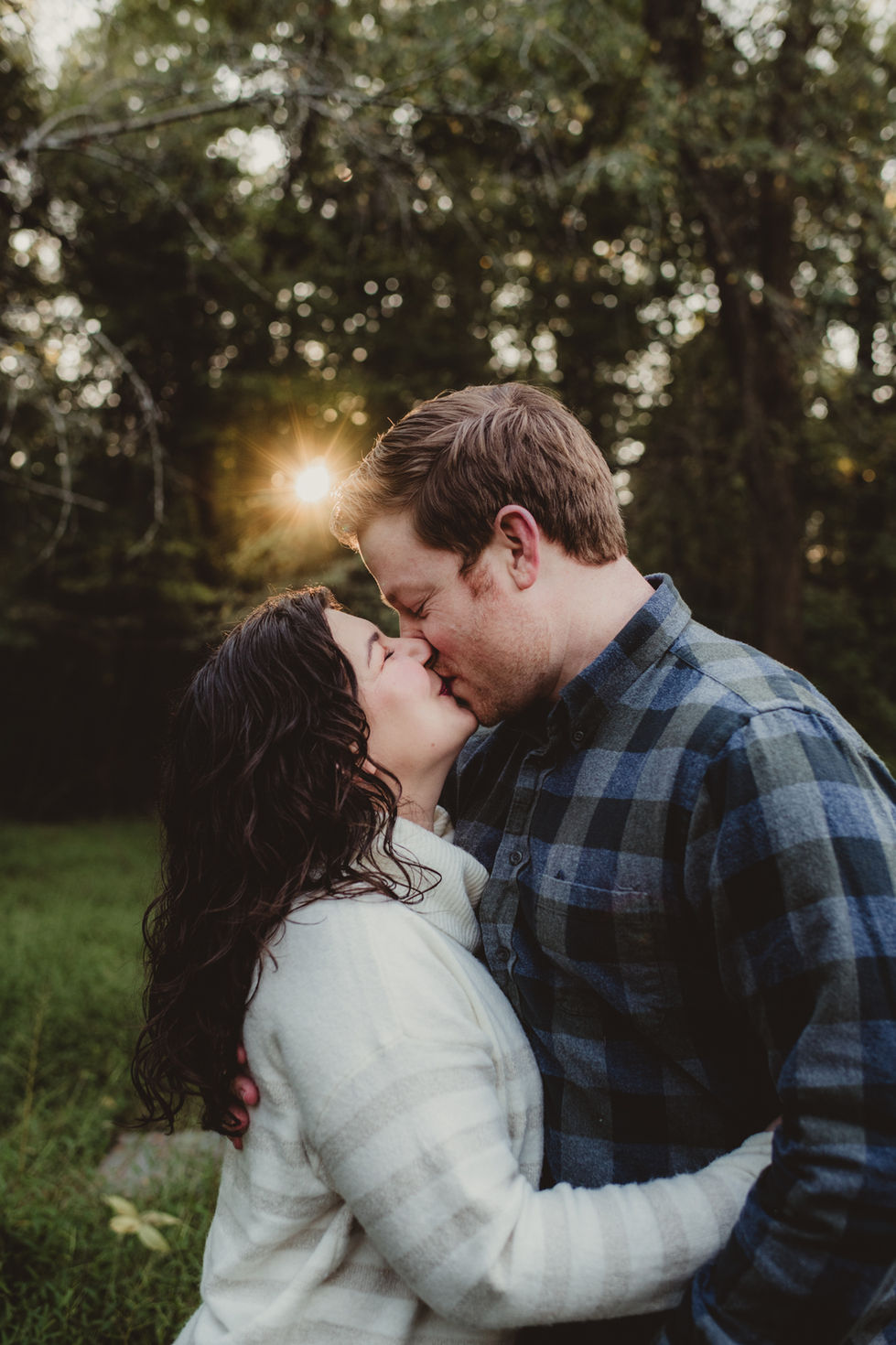 Couple kissing in a forest with sunlight behind.